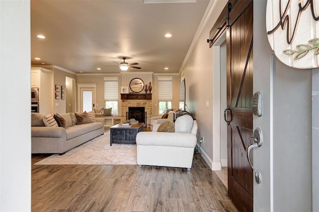 2201 Creek Side Cir, Moore, OK 73160 - living room with a barn door, ornamental molding, wood finished floors, recessed lighting, and a stone fireplace