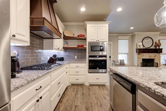 2201 Creek Side Cir, Moore, OK 73160 - kitchen featuring appliances with stainless steel finishes, custom range hood, crown molding, light stone countertops, and open shelves