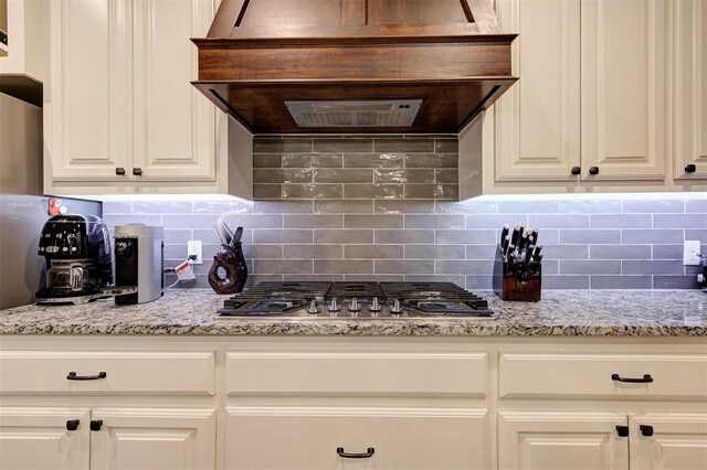 2201 Creek Side Cir, Moore, OK 73160 - kitchen featuring stainless steel gas stovetop, decorative backsplash, white cabinetry, and wall chimney exhaust hood
