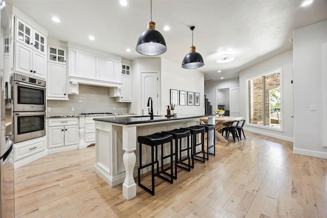 kitchen featuring decorative backsplash, a kitchen bar, a sink, stainless steel appliances, and white cabinetry