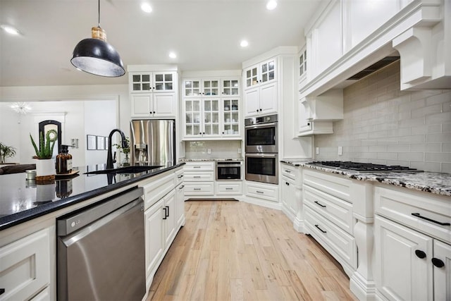 kitchen with pendant lighting, tasteful backsplash, a sink, light wood-style floors, and stainless steel appliances