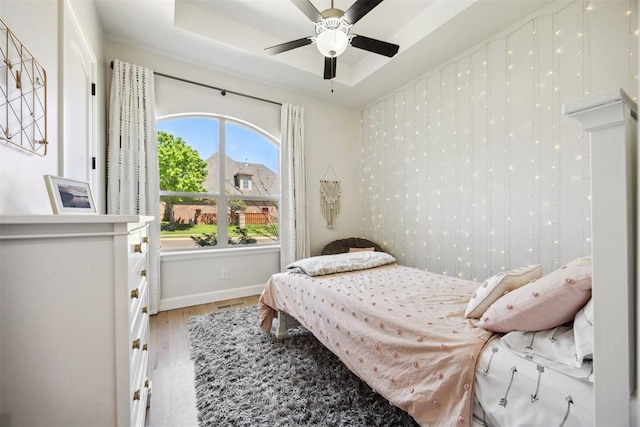 bedroom featuring baseboards, a ceiling fan, light wood-style flooring, and a tray ceiling