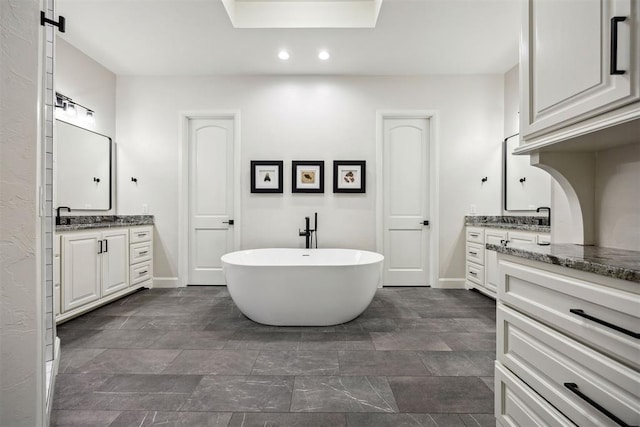 bathroom with baseboards, recessed lighting, a freestanding bath, two vanities, and stone finish flooring