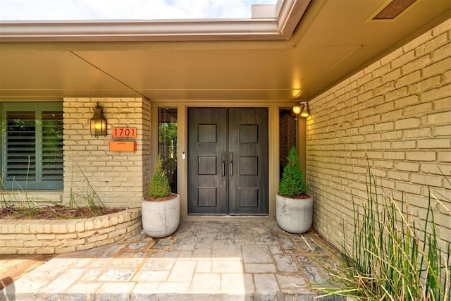 doorway to property with brick siding, visible vents, and covered porch