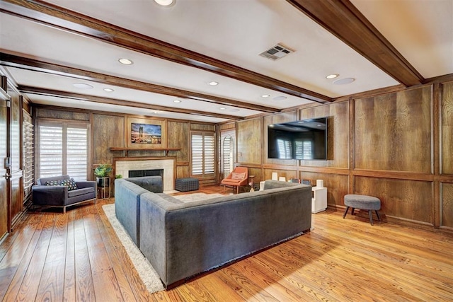 living area with visible vents, beam ceiling, wooden walls, light wood finished floors, and a premium fireplace