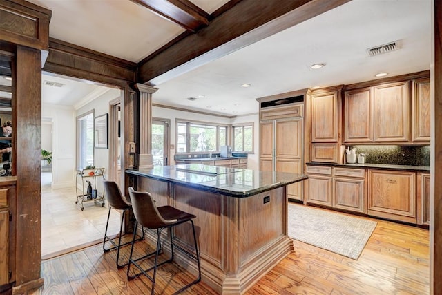 kitchen featuring a kitchen breakfast bar, paneled refrigerator, a kitchen island, backsplash, and ornamental molding