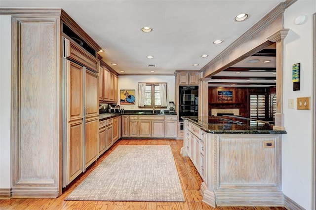 kitchen with dobule oven black, light brown cabinetry, a sink, dark stone countertops, and light wood finished floors