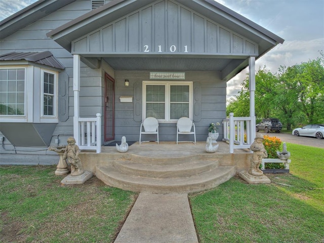 view of exterior entry with board and batten siding, a yard, and a porch
