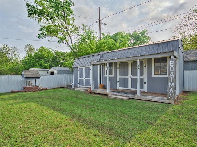 rear view of house featuring a lawn, a fenced backyard, an outbuilding, and metal roof