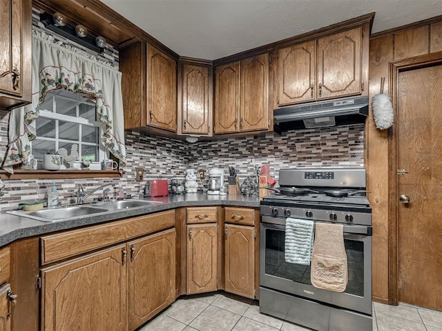 kitchen featuring tasteful backsplash, a sink, light tile patterned floors, stainless steel range with gas cooktop, and under cabinet range hood