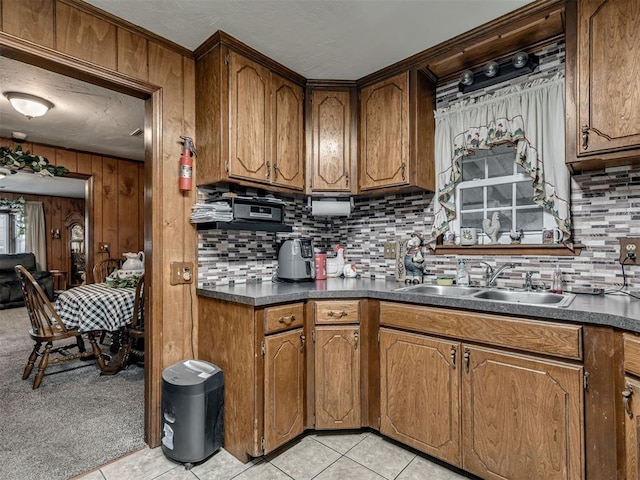 kitchen featuring light tile patterned flooring, dark countertops, brown cabinets, tasteful backsplash, and a sink