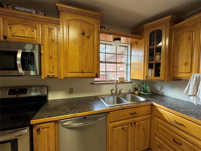 kitchen featuring stainless steel appliances, dark countertops, glass insert cabinets, and a sink