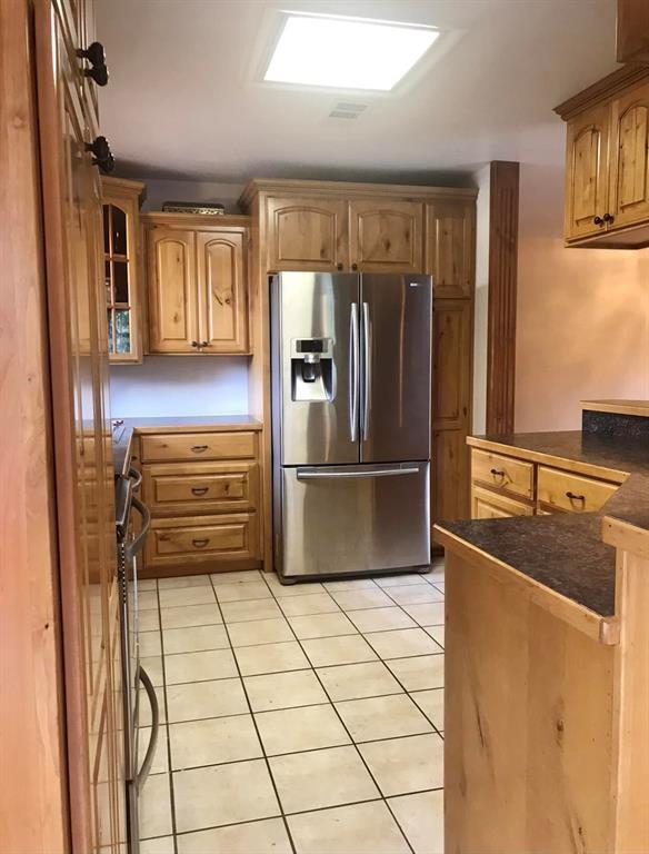 kitchen with stainless steel refrigerator with ice dispenser, range, dark countertops, light tile patterned floors, and a peninsula