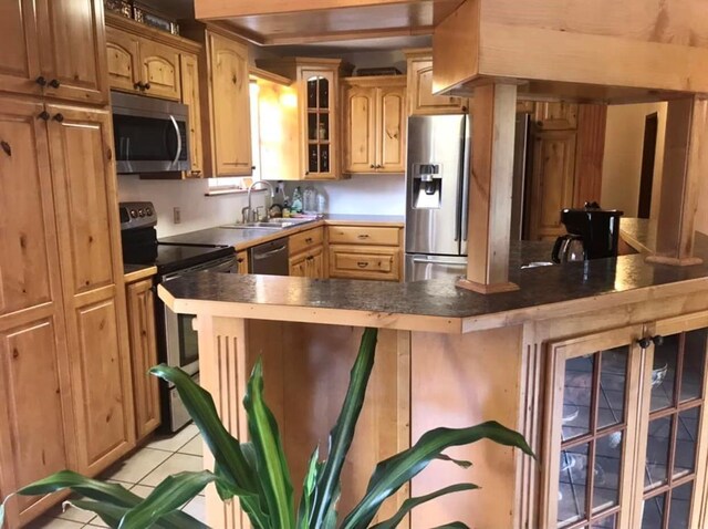 kitchen featuring light tile patterned flooring, appliances with stainless steel finishes, a sink, a breakfast bar area, and glass insert cabinets