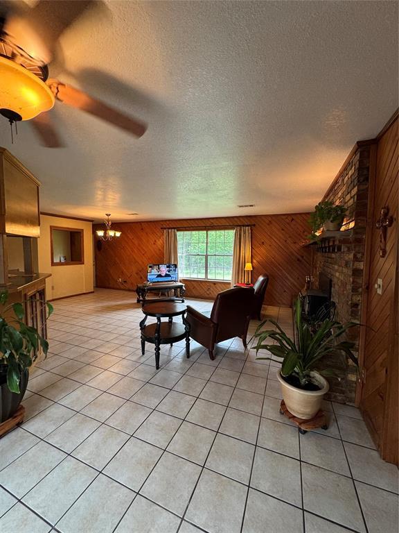 living room featuring light tile patterned floors, ceiling fan with notable chandelier, wood walls, and a textured ceiling