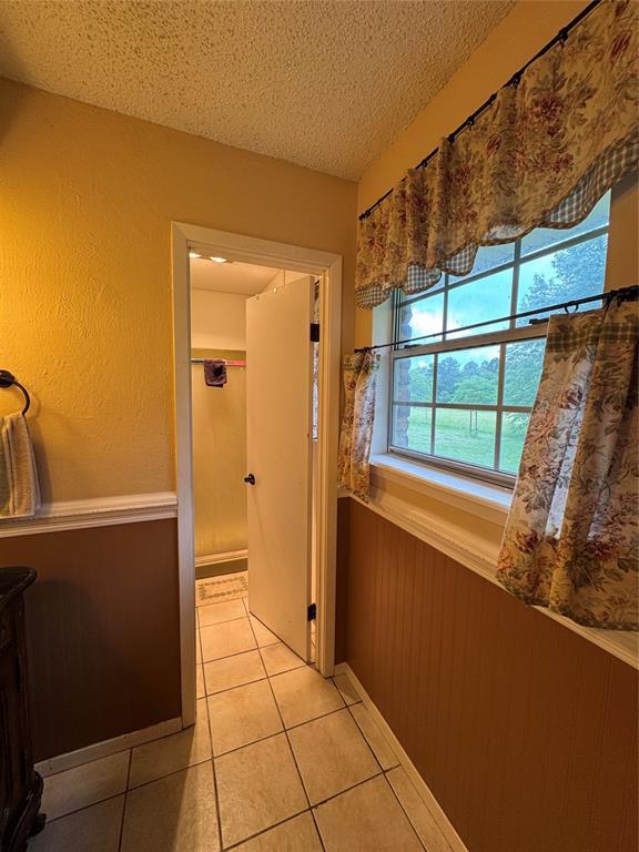 hall featuring a textured ceiling, light tile patterned floors, and wainscoting