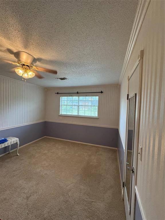 unfurnished bedroom featuring crown molding, a textured ceiling, visible vents, and carpet floors