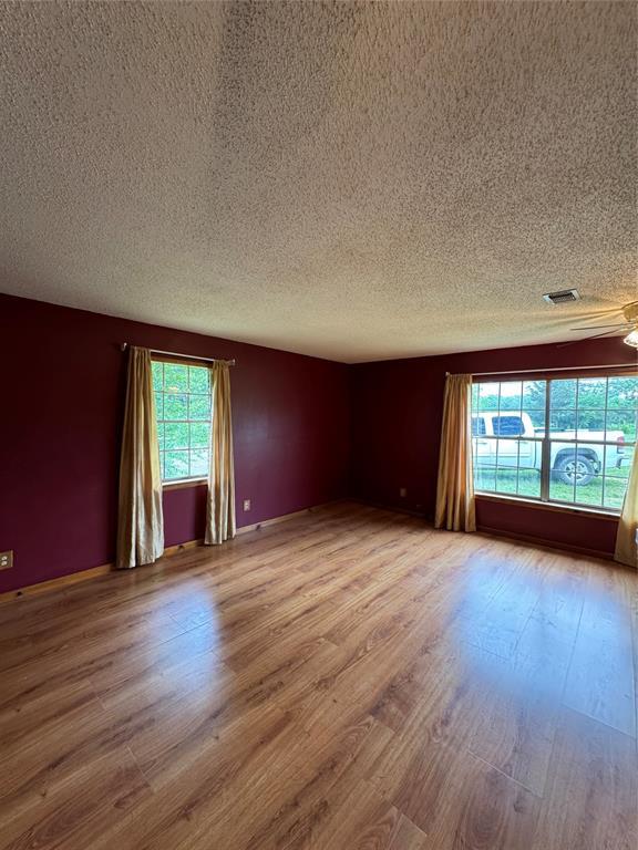 empty room with wood finished floors, a textured ceiling, and visible vents
