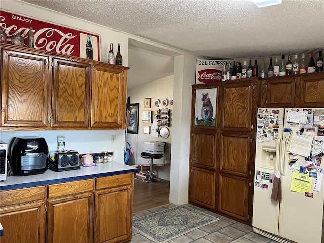 kitchen with brown cabinetry, light countertops, a textured ceiling, and white fridge with ice dispenser