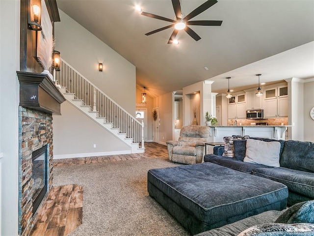 living room with a fireplace, high vaulted ceiling, a ceiling fan, baseboards, and stairway