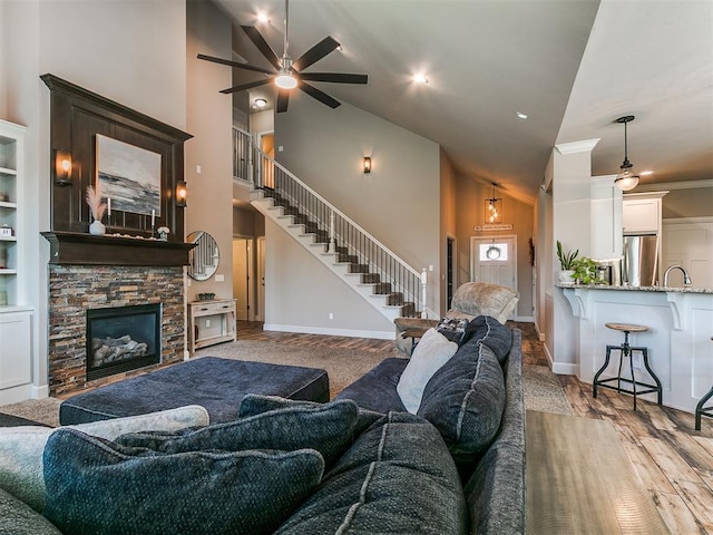 living room featuring stairs, a ceiling fan, high vaulted ceiling, and baseboards