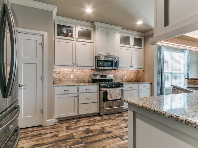 kitchen featuring appliances with stainless steel finishes, backsplash, light stone counters, and dark wood-type flooring