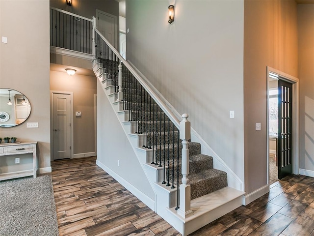 stairs with baseboards, wood finished floors, and a towering ceiling