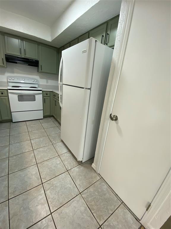 kitchen with green cabinetry, light tile patterned floors, white appliances, and under cabinet range hood