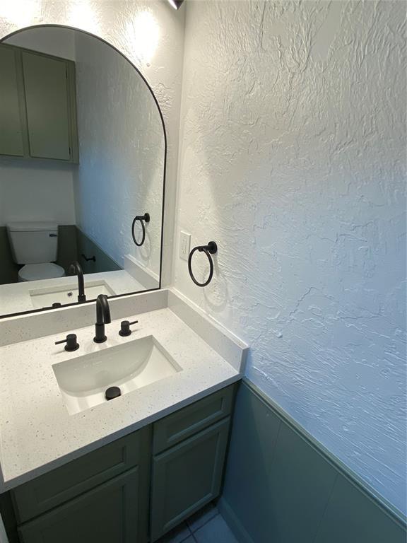half bath featuring toilet, a textured wall, and vanity