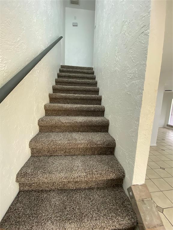 stairs with tile patterned floors, visible vents, and a textured wall