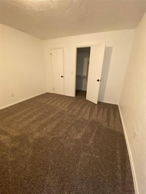 spare room with baseboards, dark colored carpet, and a textured ceiling