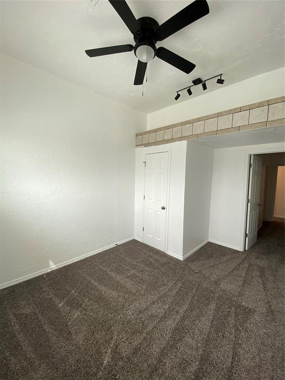 unfurnished bedroom featuring track lighting, ceiling fan, carpet, and baseboards