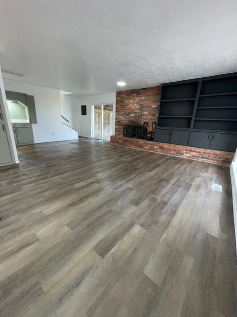 unfurnished living room featuring a textured ceiling, wood finished floors, and a brick fireplace
