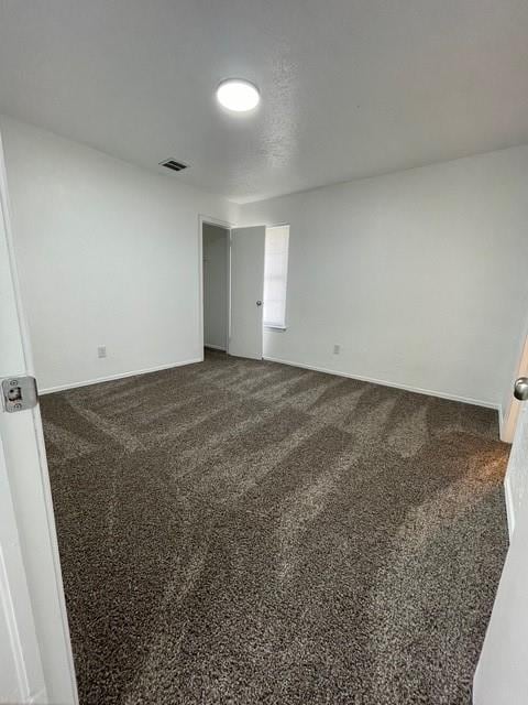 spare room with visible vents, dark carpet, and baseboards