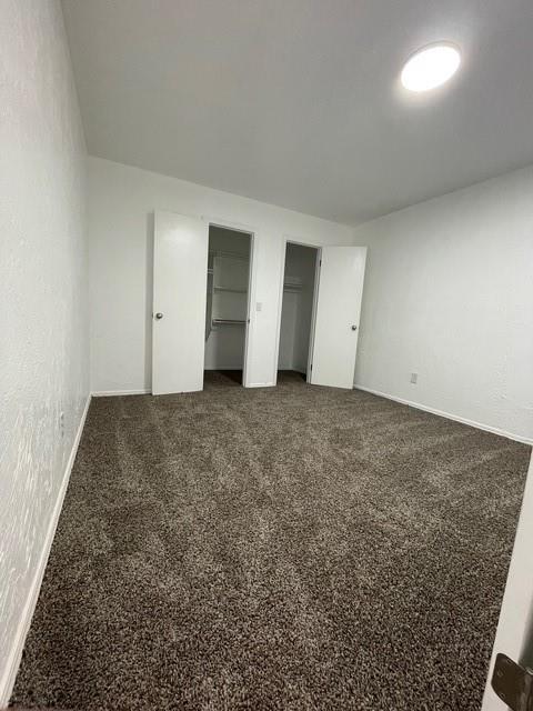 unfurnished bedroom featuring two closets, carpet flooring, and baseboards