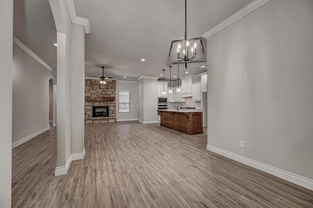 11608 NW 104th St, Yukon, OK 73099 - unfurnished living room with crown molding, arched walkways, light wood finished floors, a fireplace, and ceiling fan with notable chandelier
