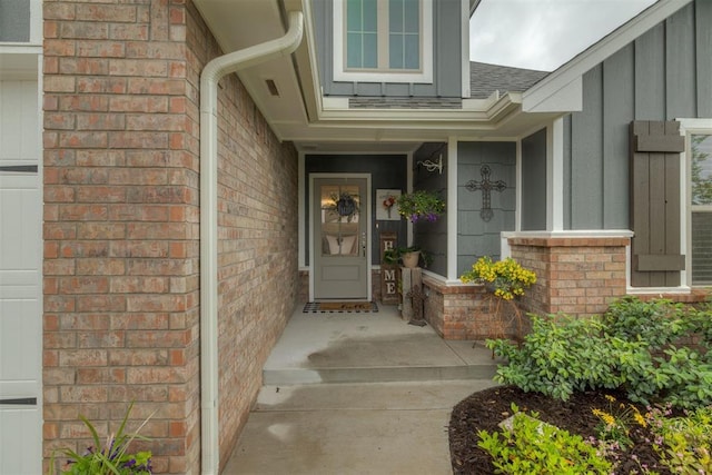 doorway to property featuring a shingled roof, board and batten siding, and brick siding