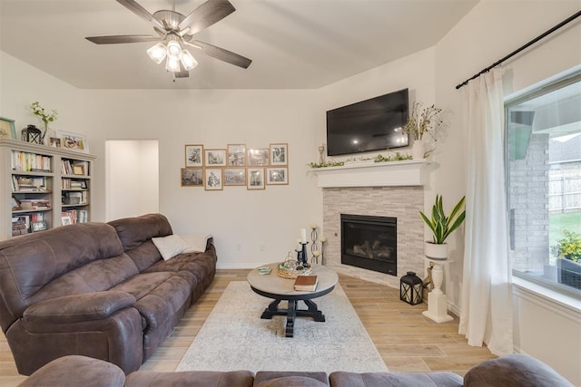 living area featuring baseboards, a glass covered fireplace, ceiling fan, and wood finished floors