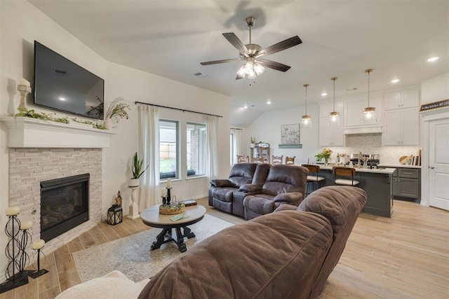 living room featuring a stone fireplace, a ceiling fan, light wood-style flooring, and recessed lighting