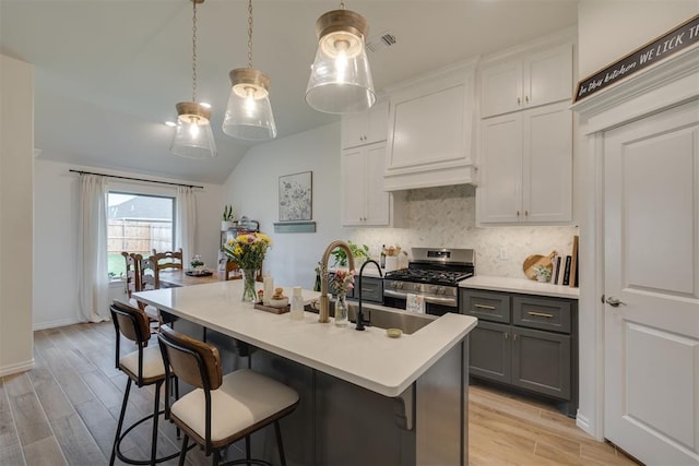 kitchen with stainless steel gas range oven, gray cabinets, light wood finished floors, and tasteful backsplash