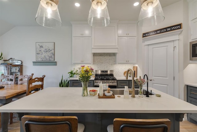 kitchen featuring stainless steel range with gas stovetop, light countertops, decorative backsplash, and a kitchen bar