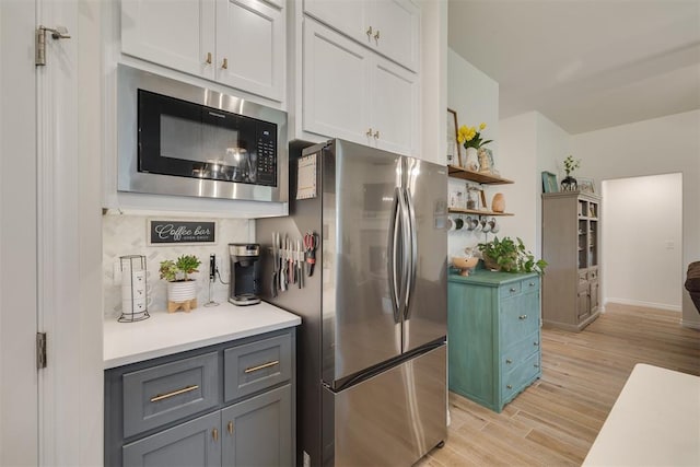 kitchen featuring black microwave, open shelves, light countertops, freestanding refrigerator, and light wood-style flooring
