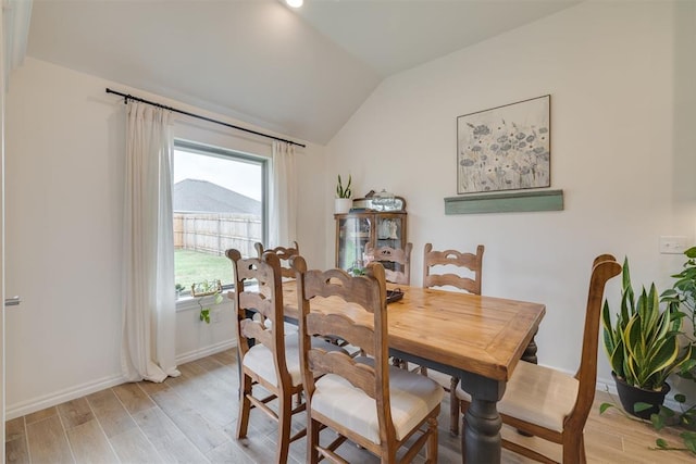 dining space with baseboards, vaulted ceiling, and light wood-style flooring