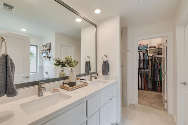 bathroom with a sink, a walk in closet, double vanity, and visible vents