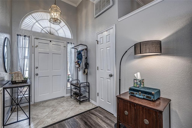 foyer entrance with crown molding, a textured wall, a notable chandelier, wood finished floors, and visible vents