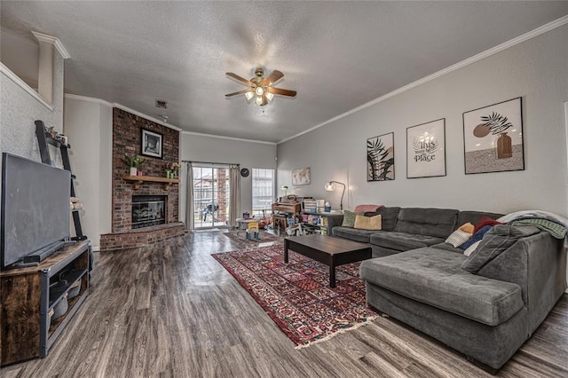 living room with ceiling fan, a brick fireplace, a textured ceiling, wood finished floors, and ornamental molding