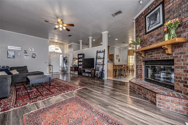 living area with a fireplace, a textured ceiling, a ceiling fan, wood finished floors, and visible vents