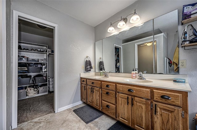 full bath with double vanity, a textured wall, a spacious closet, and a sink