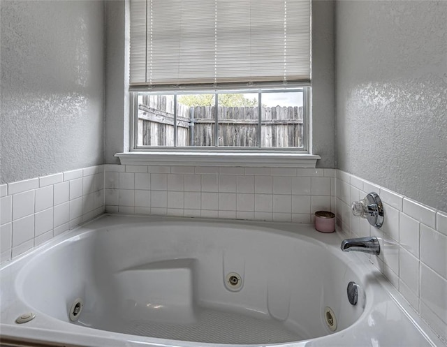 bathroom featuring a textured wall and a tub with jets