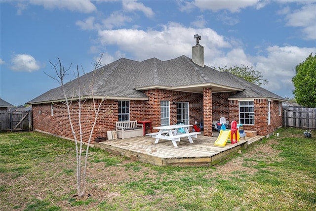 rear view of property featuring a fenced backyard, roof with shingles, a deck, and brick siding